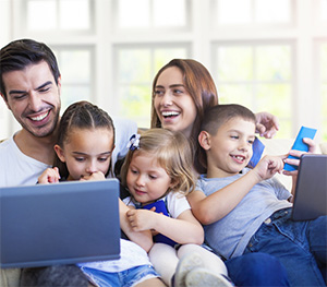 En familj sitter i soffan och håller i telefoner och en dator